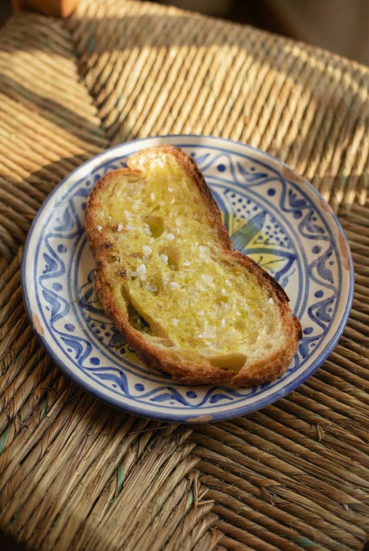 Scheibe warmes Sauerteigbrot mit LA OLIF Olivenoel und grobem Salz auf einem blau gemusterten Keramikteller